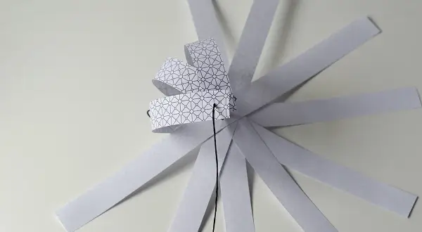 Papierowa ozdoba choinkowa 3D w trakcie tworzenia, z pasków z geometrycznym wzorem.